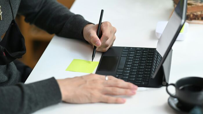 Person writing on a sticky note next to a laptop, illustrating work secrets related to barista, doctor, and plumber professions.