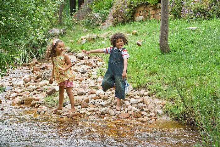 Two children playing barefoot by a rocky stream, enjoying nature and experiencing a real-life horror story moment.