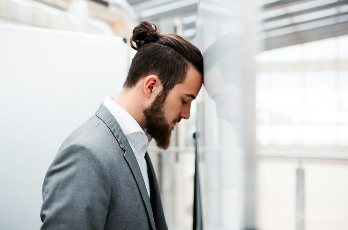 Man in gray suit with beard and bun leaning head against glass, illustrating funny steak and lobster complaints.