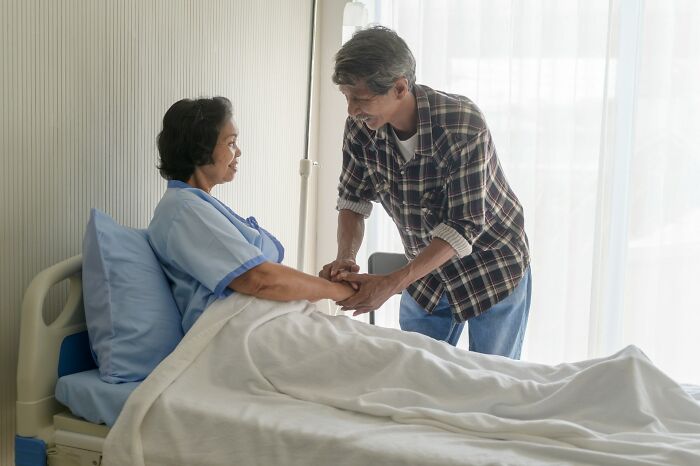 Man holding hands with woman in hospital bed, sharing emotional moment and heavy confessions conversation.