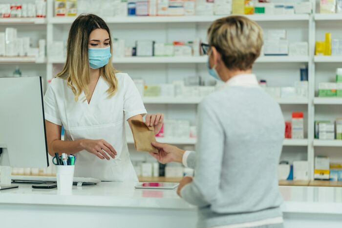 Pharmacist wearing mask hands a medication bag to a customer in a pharmacy, illustrating examples of Karens so crazy.
