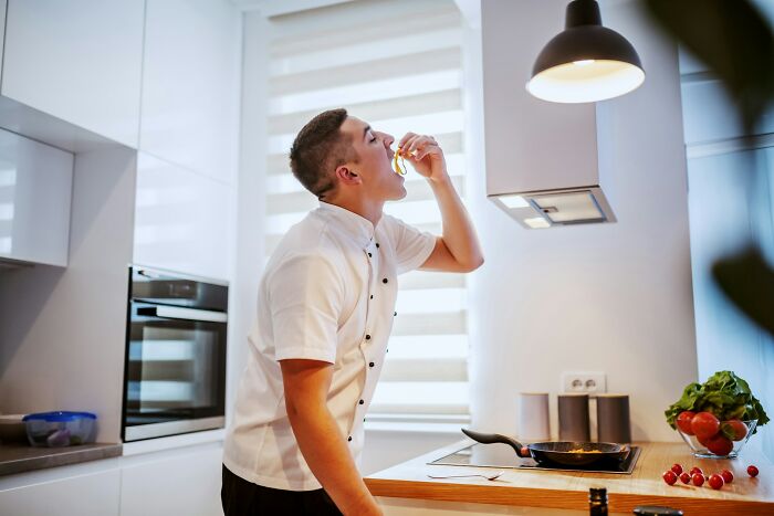 Chef tasting food in a modern kitchen, highlighting common mistakes home cooks make, including the need to sharpen knives.