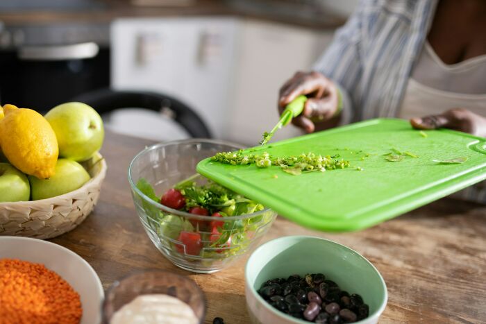 Home cook preparing fresh salad, using a cutting board to transfer chopped herbs, highlighting knife sharpening tips.