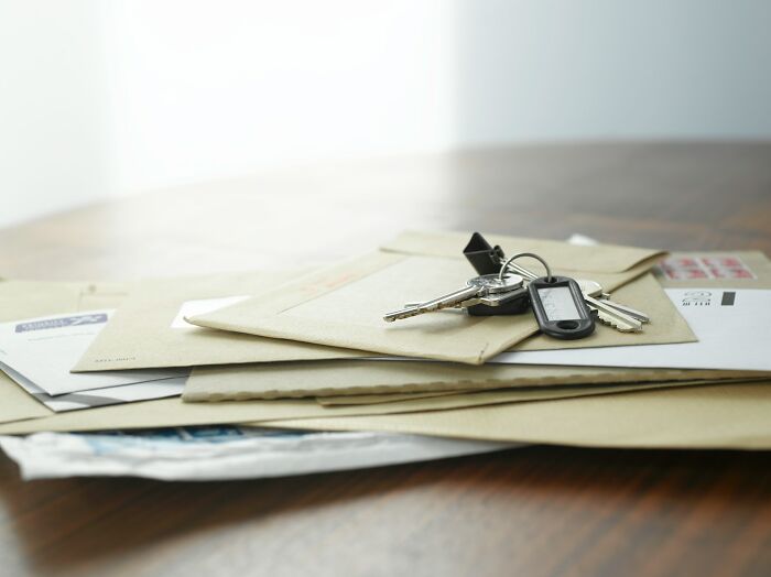 Stack of envelopes on a wooden table with keys resting on top, illustrating common items mistaken as a scam by internet users.