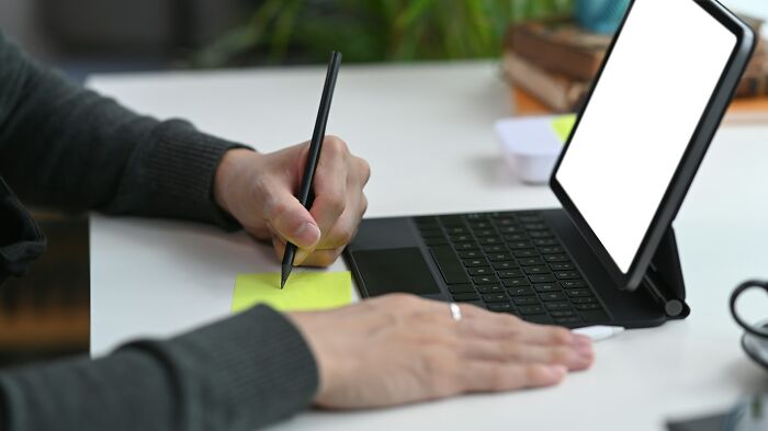 Person writing notes on a sticky pad next to a tablet with keyboard, researching the etymology of common words.