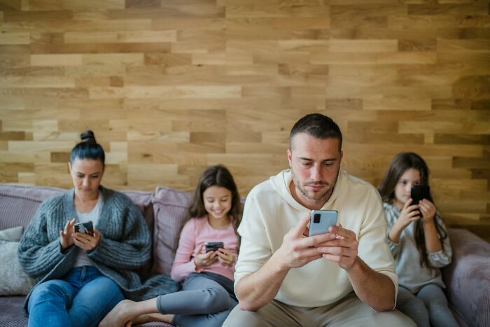 Family on couch ignoring each other while using smartphones, illustrating common ways parents fail at raising kids.