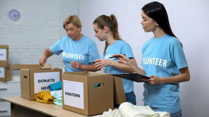 Three volunteers sorting donations into boxes labeled for donating, illustrating common misconceptions about scams.