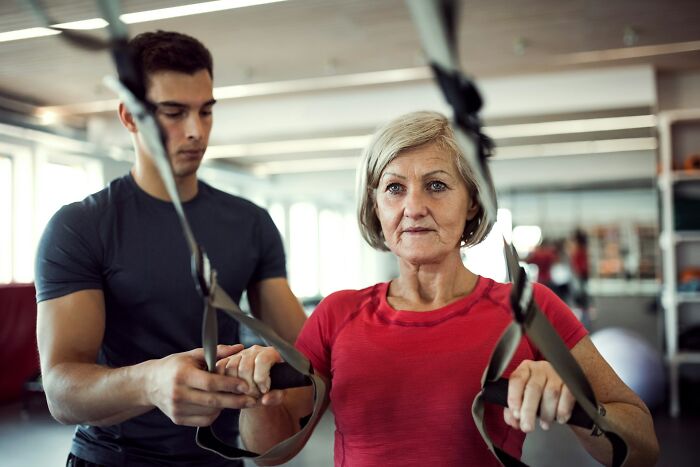 Personal trainer assisting mature woman with resistance training at gym, illustrating common internet users’ misconceptions about scams.