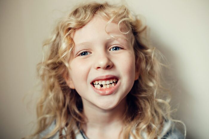 Smiling child with curly blonde hair and a missing tooth, capturing a moment of humor and accidental hurt in loved ones.