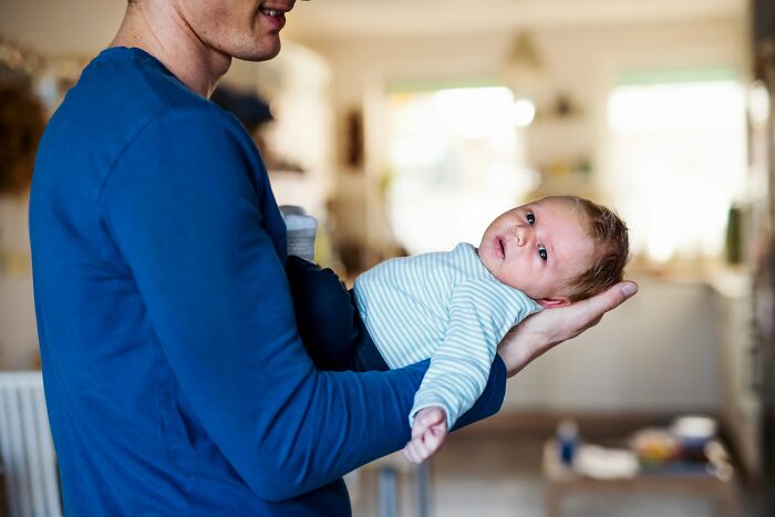 Man in blue shirt holding baby in striped onesie indoors, symbolizing family dynamics and golden child stories.