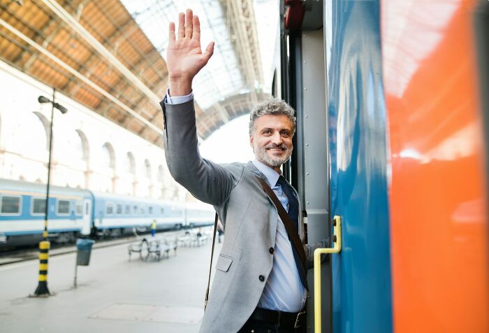 Man waving from train doorway at station, illustrating people explaining the etymology of common words concept.