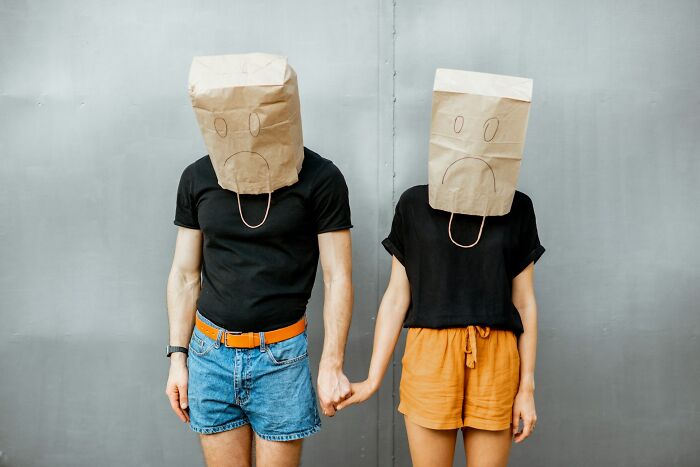 Two people wearing paper bags with sad faces, holding hands, illustrating unusual childhood habits realization.