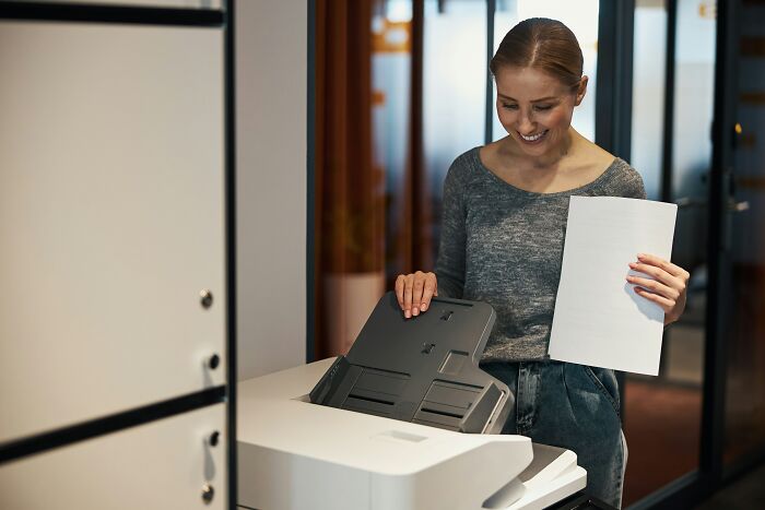 Woman printing documents at office printer, illustrating infuriating examples of we’ve always done it this way at work.