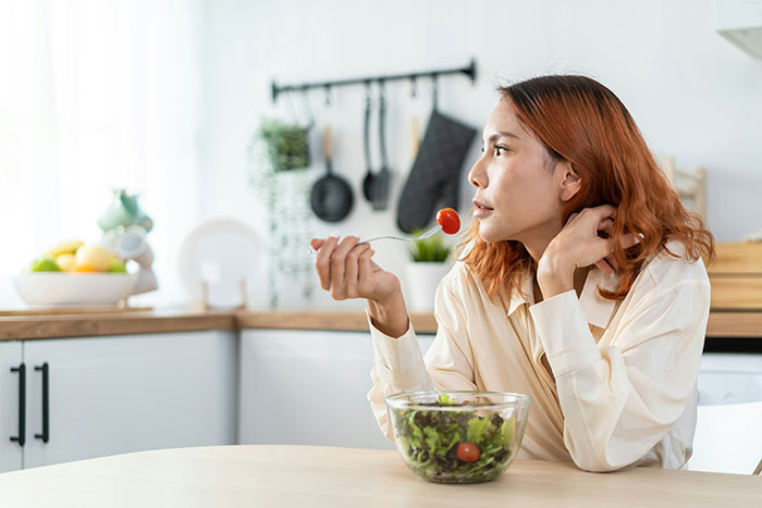 Woman eating salad in kitchen, reflecting on domestic chores and no longer playing mommy in household duties.
