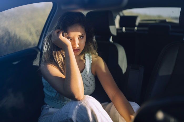 Young woman sitting in car looking upset and reflective, illustrating a guy learning that his friend likes him.