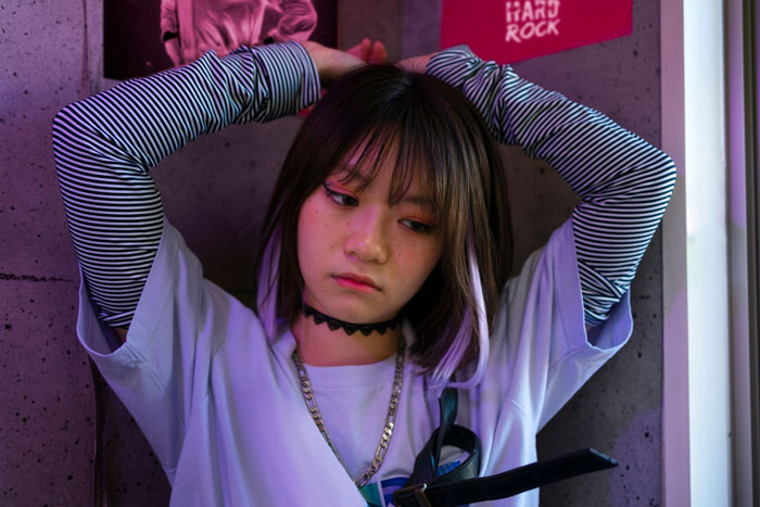 Young woman looking upset after being mocked for fangirling over a K-Pop band in a public setting.