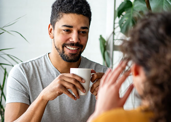 Man smiling and holding a cup while on a date, capturing a moment in a daughter&rsquo;s relationship affected by a mom&rsquo;s actions.