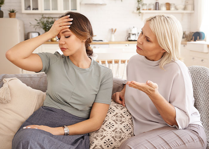 Mother and daughter having a tense conversation on a couch, illustrating mom destroys daughter&rsquo;s happy relationship after date.