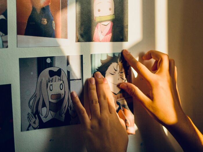 Hands placing anime pictures on a wall, illustrating the butterfly effect concept in real life moments.