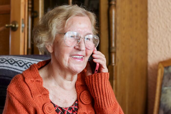 Older woman wearing glasses and orange sweater talking on phone, illustrating times people fell for scams and their effects.