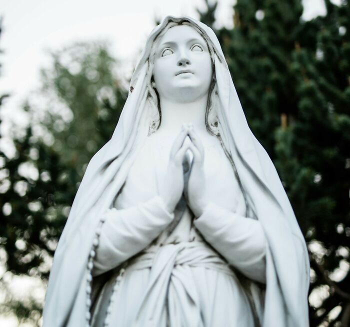 White statue of a praying woman with a veil, captured in an outdoor setting, eerie and unsettling surveillance camera image.