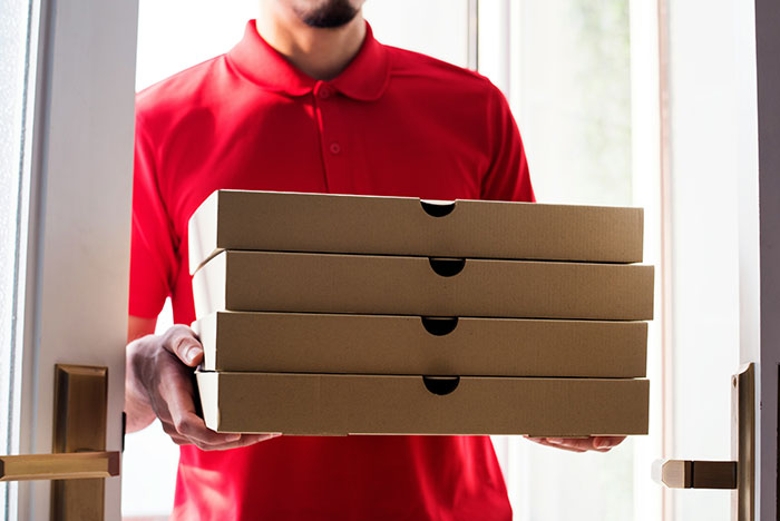 Delivery person in red shirt holding three pizza boxes at an open door, illustrating moments gut instinct was correct.