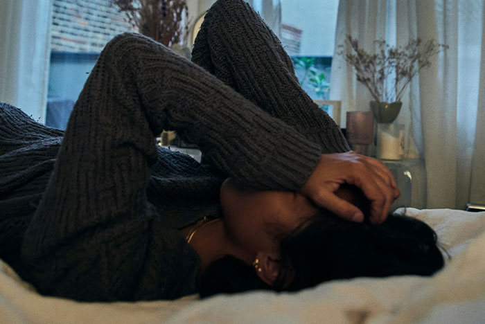 Person lying down in dimly lit room, covering face with arm, capturing a moment of gut instinct being 100% correct.