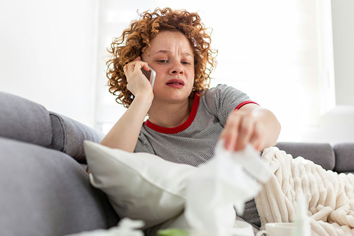 Woman with curly hair on a phone call, showing gut instinct while reaching for tissues on a couch at home.