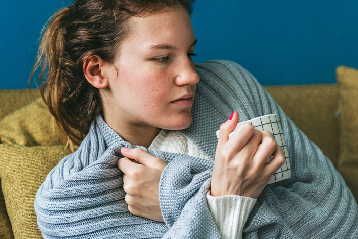 Young woman wrapped in a blanket holding a mug, reflecting on moments their gut instinct was 100 percent correct.