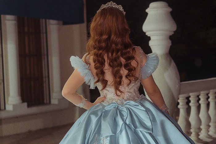 Young woman in a blue ball gown and tiara standing on a balcony, capturing a moment of instinct and confidence.