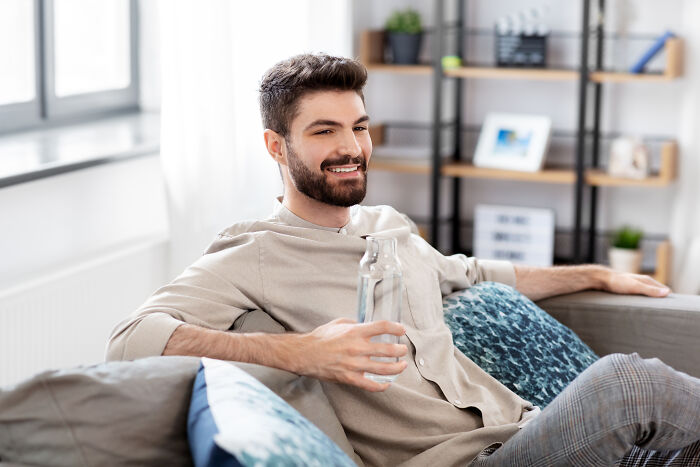 Young man relaxing on a couch holding a water bottle, reflecting feelings adopted people often understand deeply.