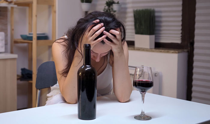 Woman showing distress while sitting at table with wine bottle and glass, depicting an evil stepmom turning to wine.