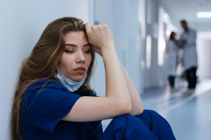 Young woman in blue scrubs sitting on floor looking tired, reflecting on life lessons and family dynamics. Young woman in blue scrubs sitting on floor looking tired, reflecting on life lessons and family dynamics.