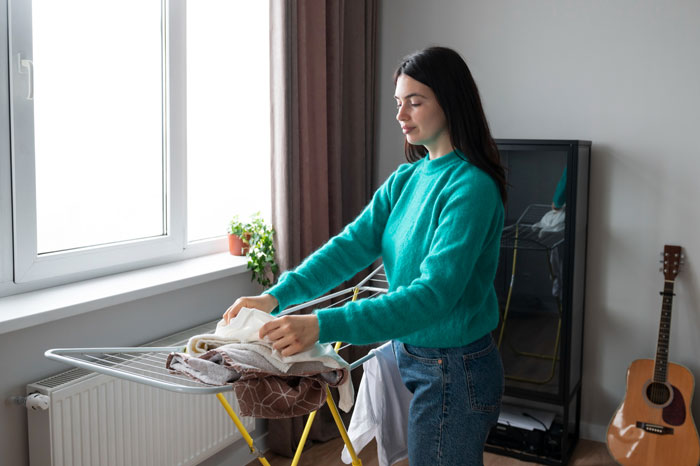 Young woman folding laundry indoors near window, illustrating golden child getting laundry service from parents. Young woman folding laundry indoors near window, illustrating golden child getting laundry service from parents.