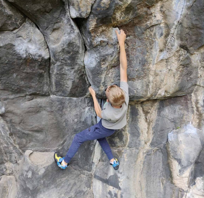 Boy rock climbing on a steep rock wall, illustrating adventurous activities related to zip-lining accidents.