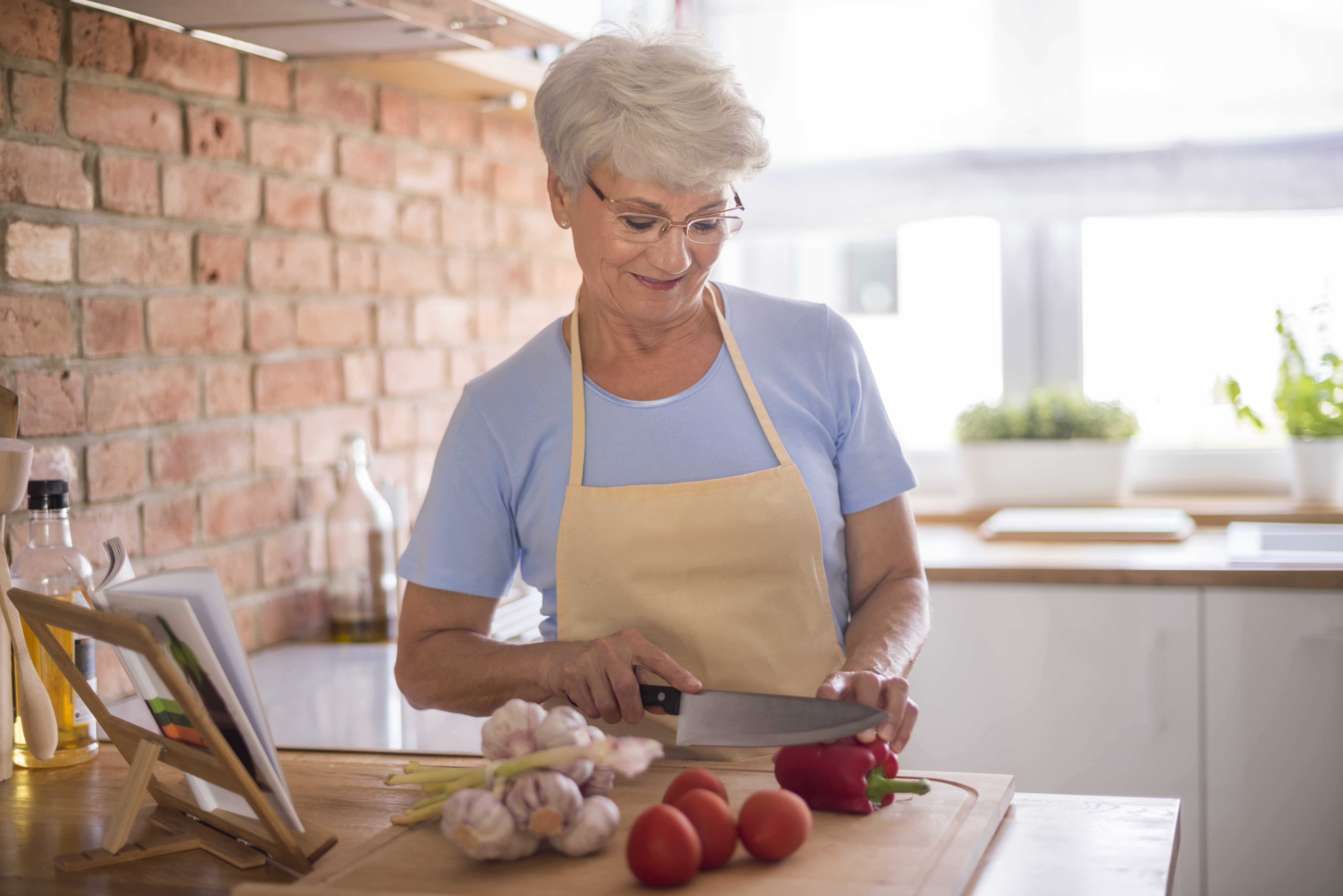 Older woman preparing vegetables in a kitchen, illustrating MIL&rsquo;s cooking concerns impacting pregnant woman&rsquo;s Thanksgiving plans.