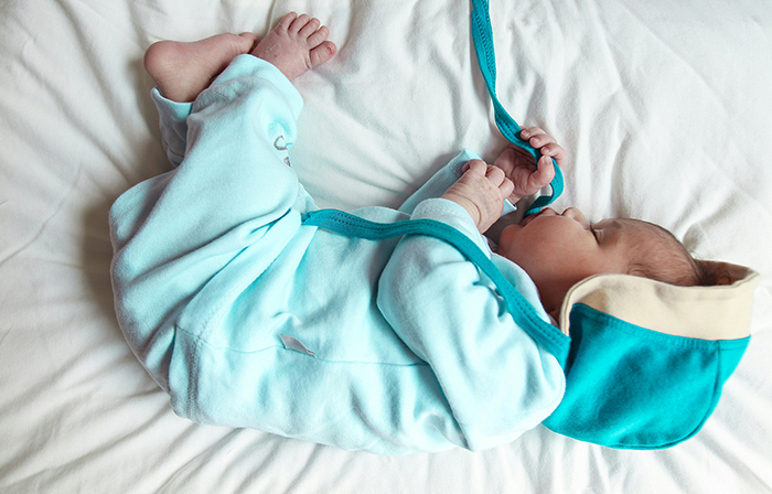 Newborn baby lying on a white bed wearing a blue outfit, symbolizing themes of pregnancy and postpartum challenges.