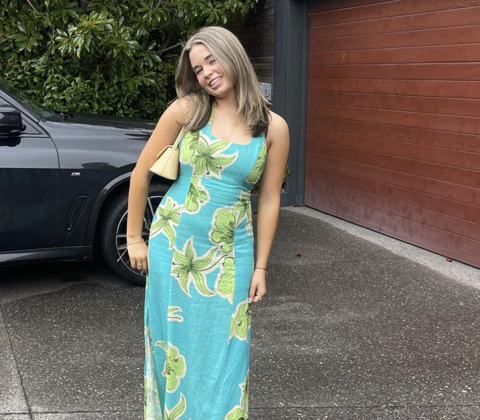 Young woman in a floral dress posing beside a black car, related to parents warning against travel after daughters' vacation loss.