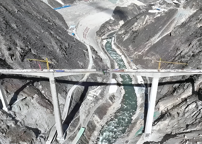 Aerial view of China’s ambitious bridge spanning a deep valley over a river, showing ongoing construction and cranes nearby. Aerial view of China’s ambitious bridge spanning a deep valley over a river, showing ongoing construction and cranes nearby.
