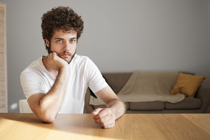 Young man with curly hair sitting thoughtfully at a wooden table, reflecting experiences only adopted people understand