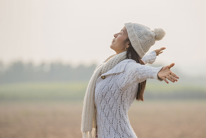 Woman wearing winter clothes with arms outstretched outdoors, representing mysteries about the human body unexplained by science.