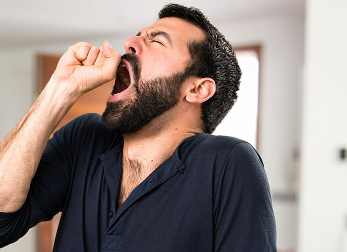 Bearded man yawning with closed eyes in a home setting illustrating mysteries about the human body science can't explain.
