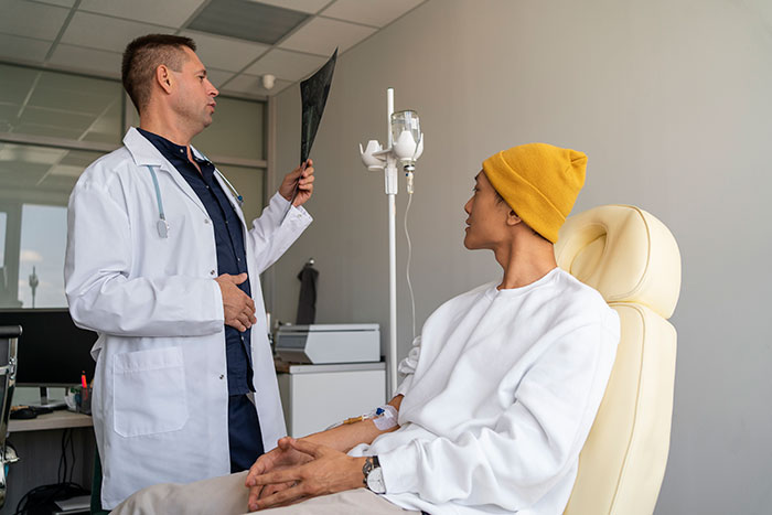 Doctor in white coat reviewing an X-ray while a patient with IV drip sits in a chair, highlighting mysteries about the human body.