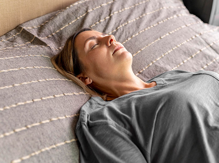 Woman resting on bed with eyes closed, illustrating mysteries about the human body that science still hasn't explained.