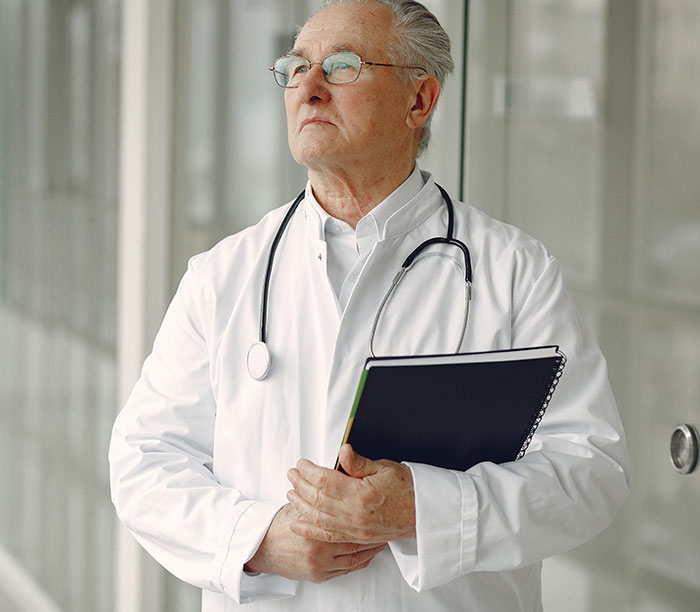 Elderly doctor in white coat with stethoscope and notebook pondering human body mysteries and medical science challenges.