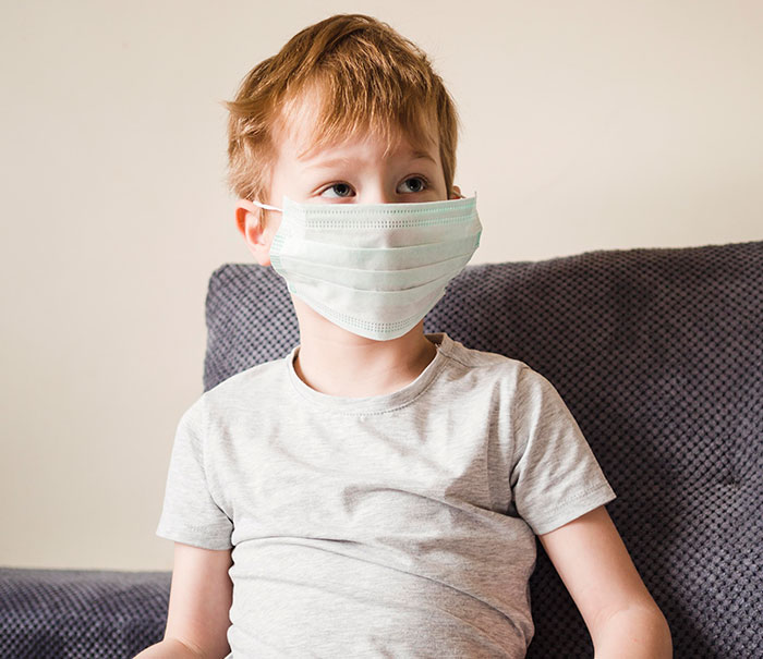 Young boy wearing a face mask sitting on a couch, highlighting mysteries about the human body science still can't explain