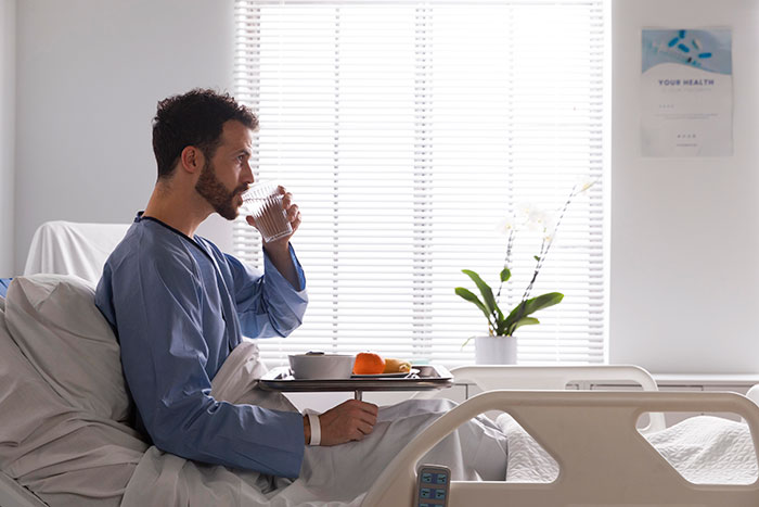 Man in hospital gown drinking water in bed, highlighting mysteries about the human body and medical science unknowns