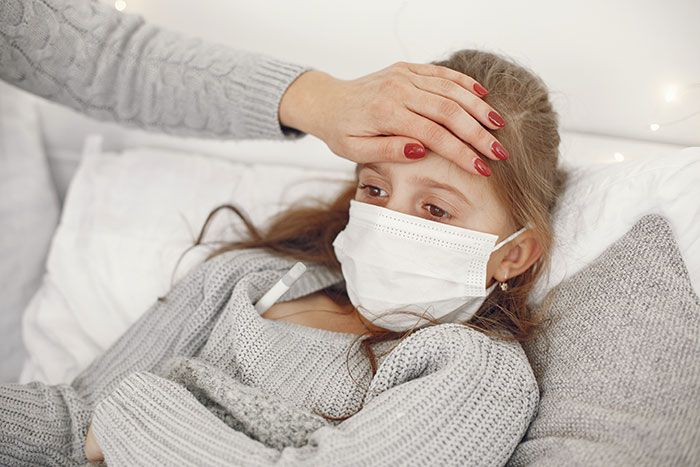 Sick girl wearing a mask in bed having her temperature checked, illustrating mysteries about the human body and health.
