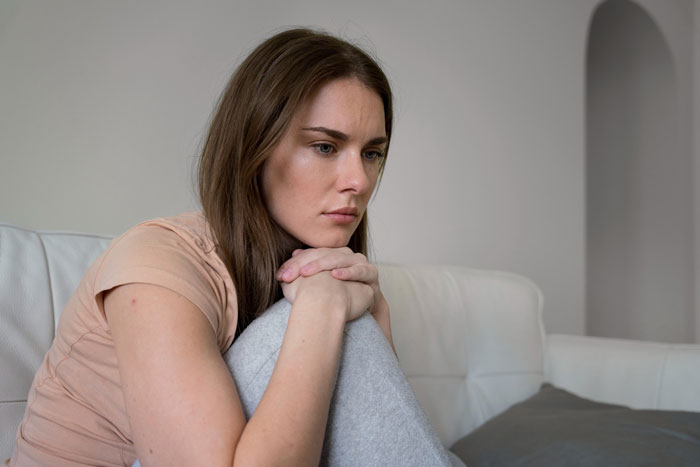 Woman sitting on couch looking pensive and overwhelmed, reflecting the challenges of caring for disabled brother. Woman sitting on couch looking pensive and overwhelmed, reflecting the challenges of caring for disabled brother.