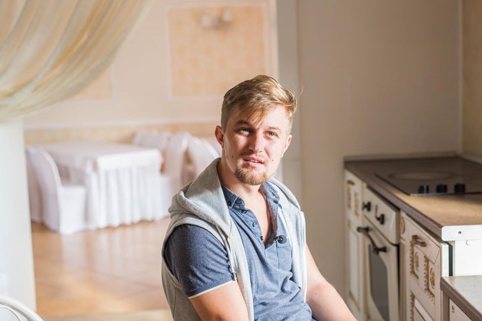 Young man sitting in a kitchen, looking troubled while caring for his disabled brother and admitting he can't handle it. Young man sitting in a kitchen, looking troubled while caring for his disabled brother and admitting he can't handle it.
